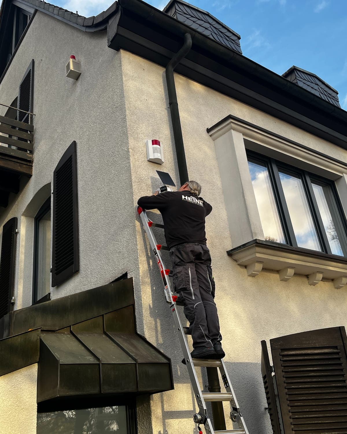 Heine-Monteur installiert eine Außensirene an einem Wohnhaus